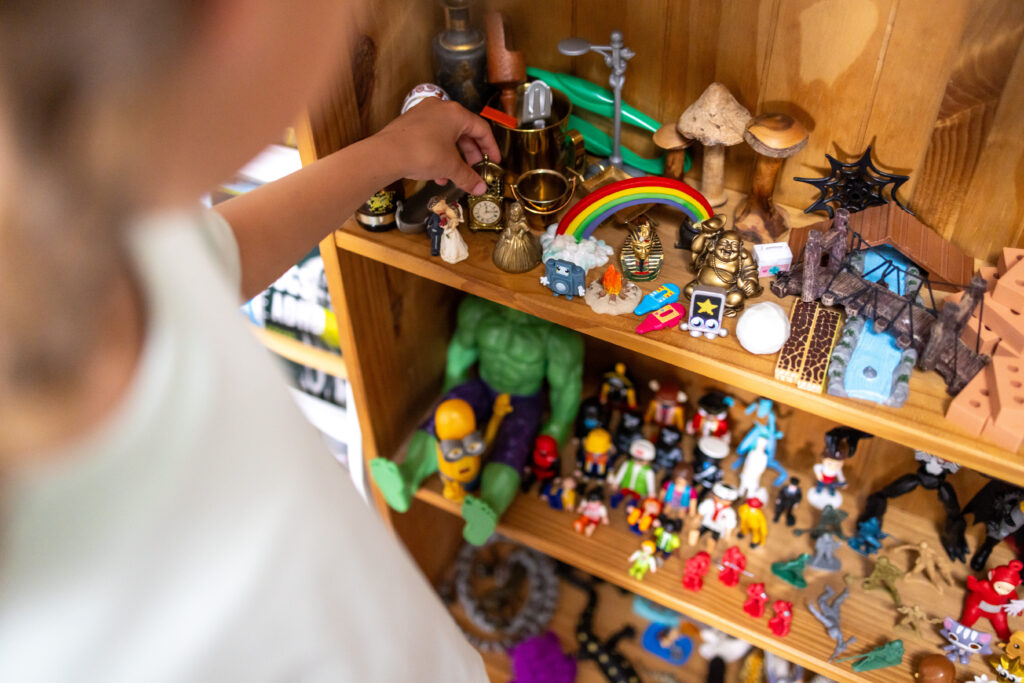 Child's hand sprinkling sand over miniature figurines in the sand tray