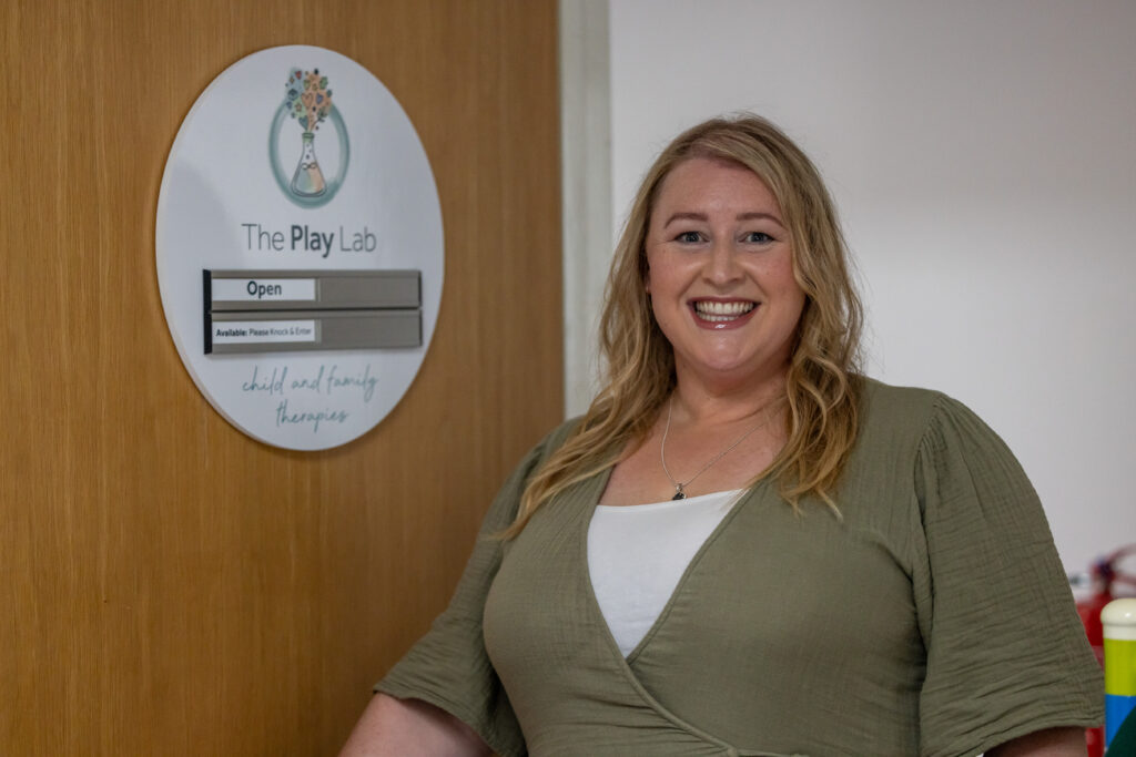 Rachel, founder of The Play Lab, smiling beside the practice door sign